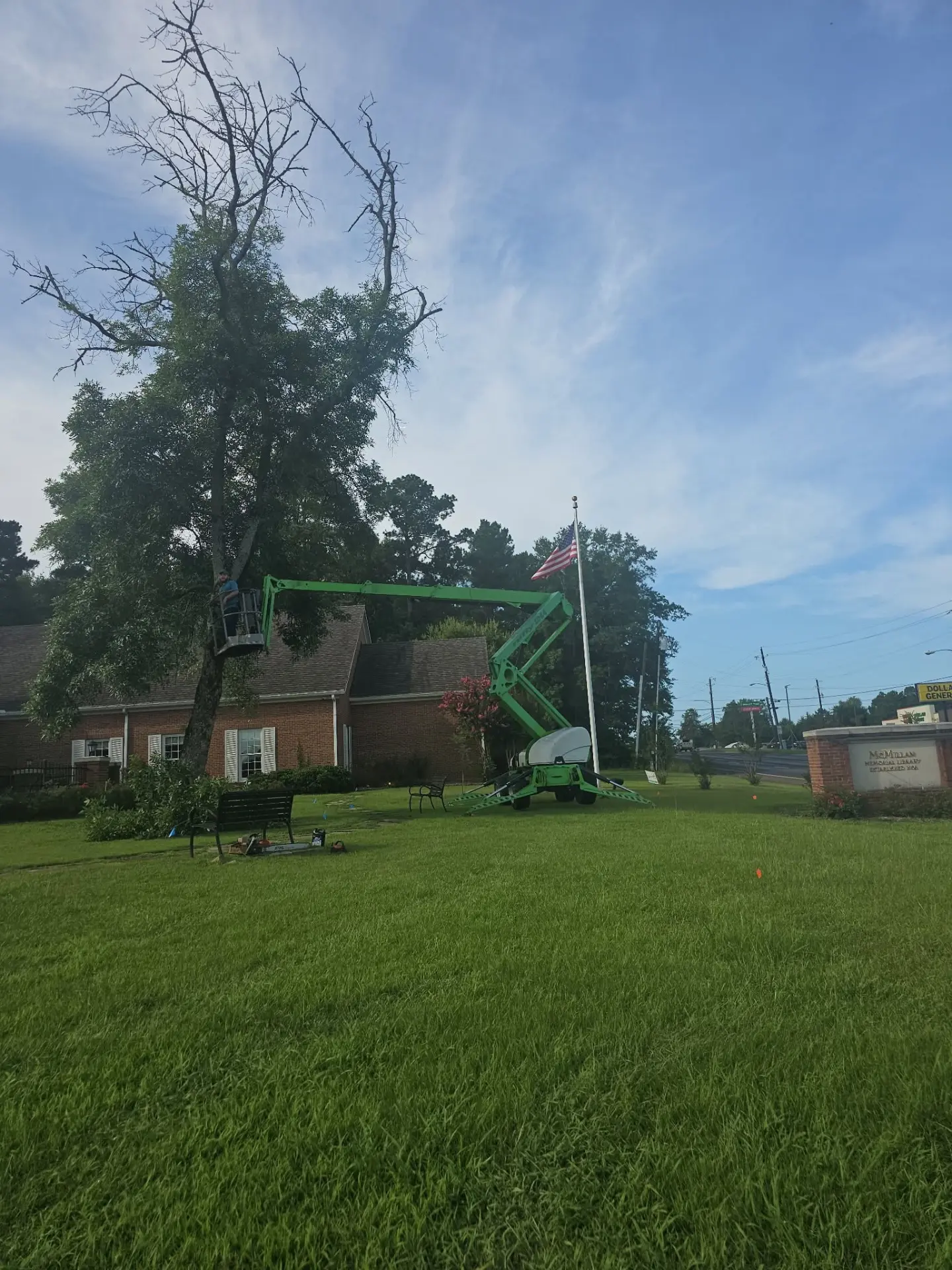 Worker in a towable boom lift trimming branches from a tall tree in front of a brick home in Overton, Texas